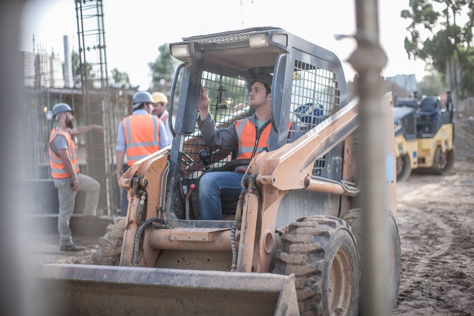 A construction worker in a skid steer machine on a jobsite.