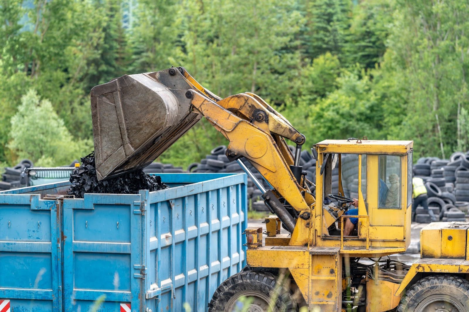 An excavator is dumping debris into a dumpster.