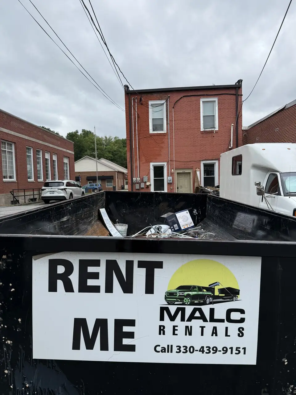 A black MALC Rentals dumpster with their number and logo in a parking lot.
