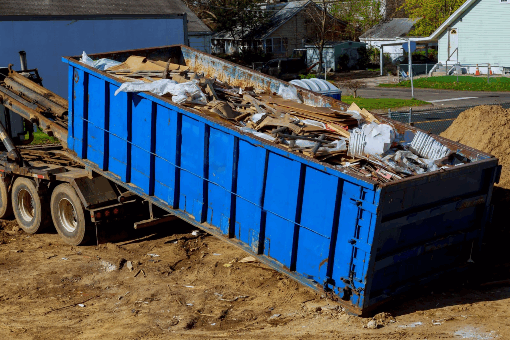 A truck is loading a full dumpster with recyclable construction waste.