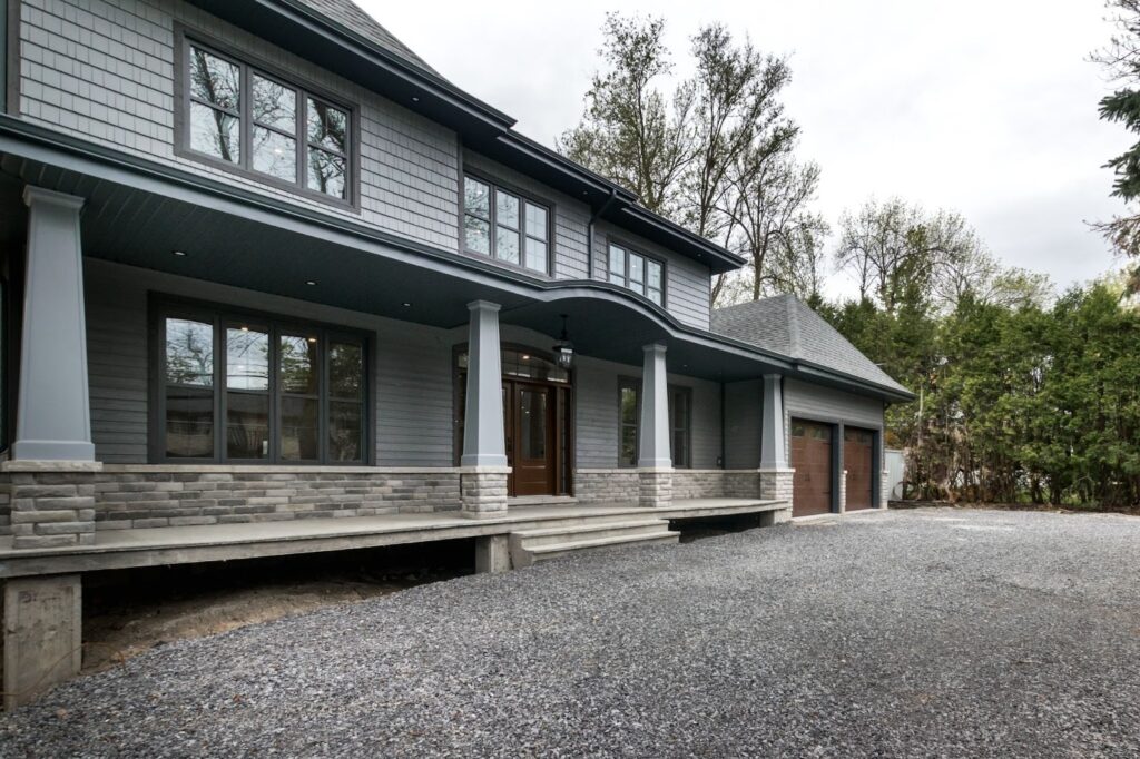 A large gray and black home with a gravel driveway.