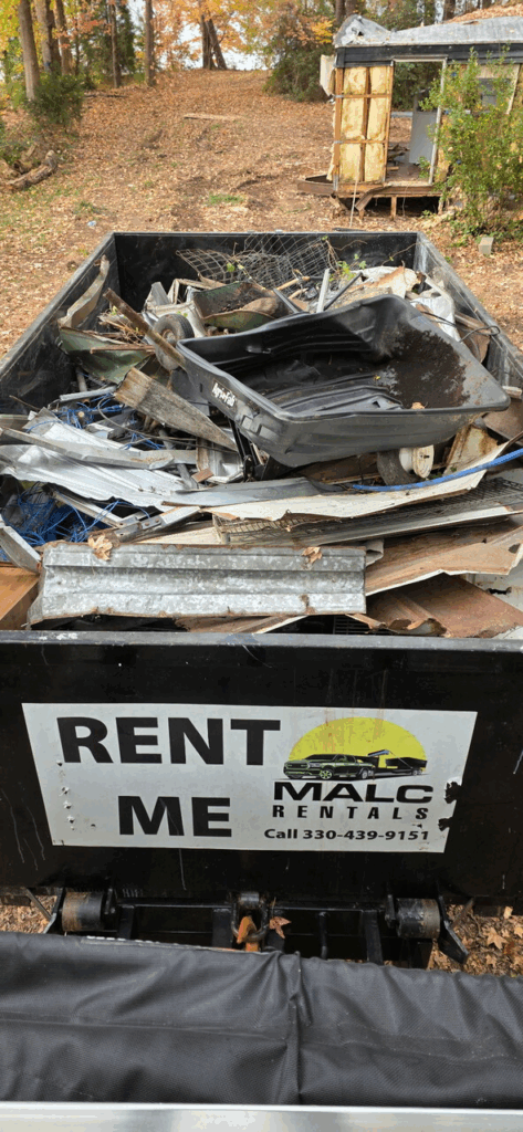 A full black MALC Rentals dumpster in the woods with their logo and number.