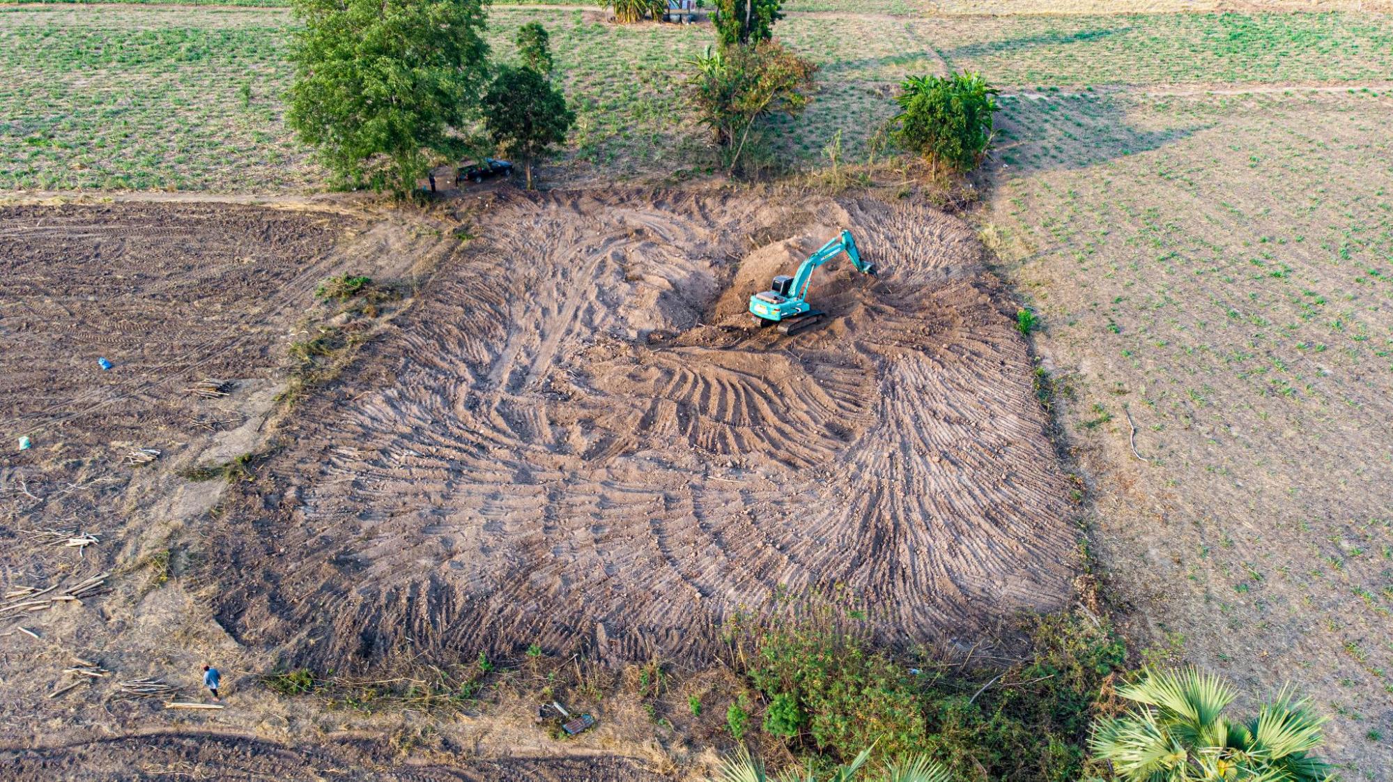 Top-down view of an excavator grading land to control water flow on a construction site.