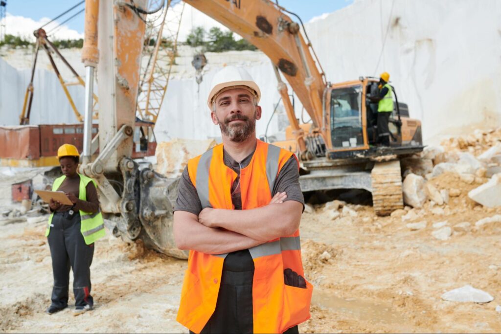 A demolition contractor stands in the foreground while other construction workers continue working in the background.